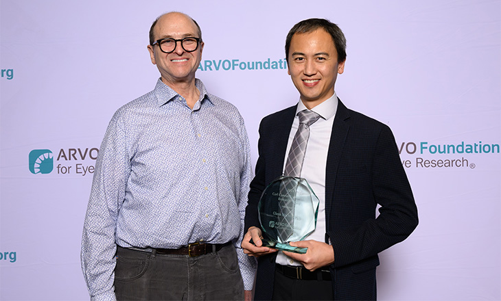 Two men stand next two each other against a lavender backdrop with the words “ARVO Foundation.” 